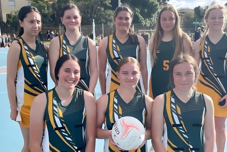Eine Gruppe junger Athletinnen des Spotswood College posiert gemeinsam auf dem Sportplatz mit einem Basketball im Vordergrund.