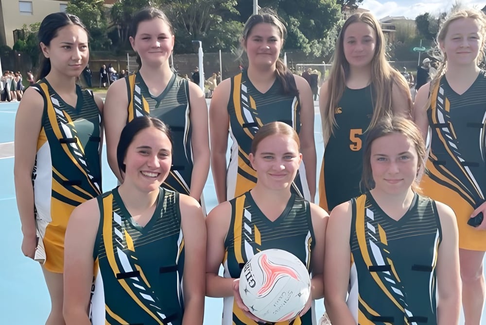 Eine Gruppe junger Athletinnen des Spotswood College posiert gemeinsam auf dem Sportplatz mit einem Basketball im Vordergrund.