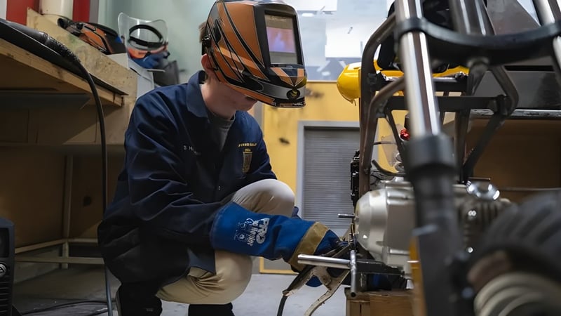 Eine Person trägt eine Schweißermaske und Schutzkleidung und arbeitet an einer Maschine in der Werkstatt des Spotswood College.