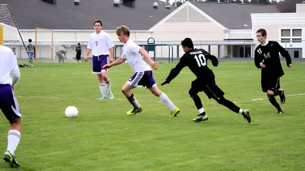 Schüler der Spring Street International School spielen ein Fußballspiel auf dem Sportplatz vor einem Schulgebäude.