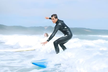 Eine Person in einem schwarzen Neoprenanzug surft auf einer Welle im Ozean mit Bergen im Hintergrund auf dem Gelände der Springbank School.