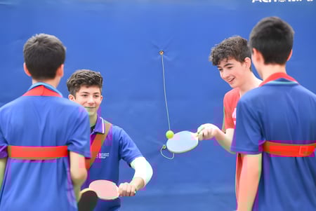 Schüler des Springbank Secondary College spielen ein Tischtennisspiel vor blauem Hintergrund.