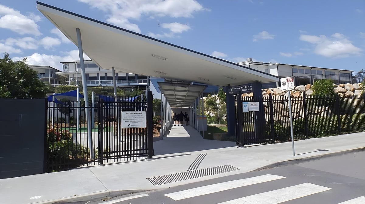 Das moderne Hauptgebäude der Springfield Central State High School mit schrägem Dach und umzäuntem Bereich ist im Vordergrund sichtbar.