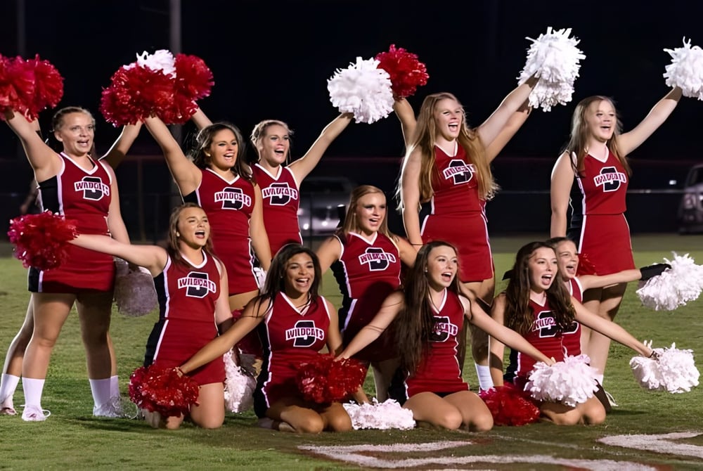 Cheerleader der Springwood School führen mit roten und weißen Uniformen eine Performance auf dem Fußballfeld bei Nacht auf.