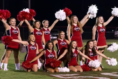 Eine Gruppe Cheerleader der Springwood School führt abends auf dem Fußballfeld eine Performance mit roten und weißen Uniformen durch.