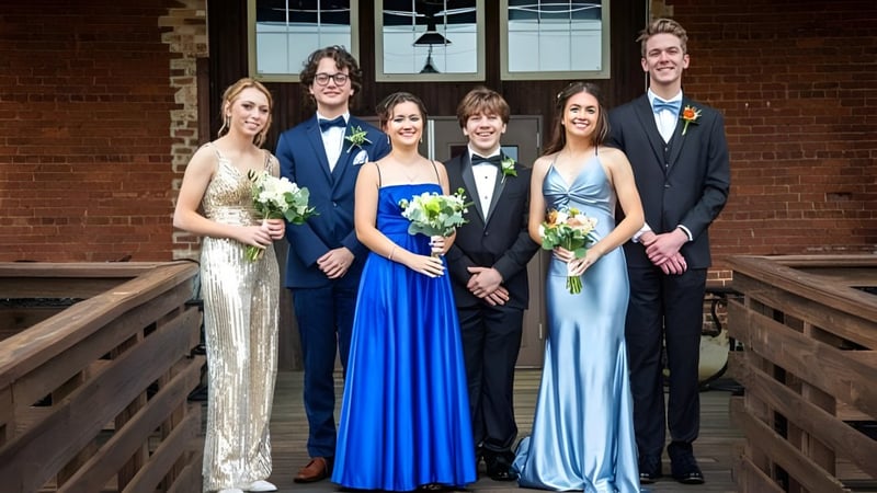 Eine Gruppe von sechs Personen in formeller Kleidung steht auf einer Holztreppe vor einem Backsteingebäude der Springwood School und hält Blumensträuße.