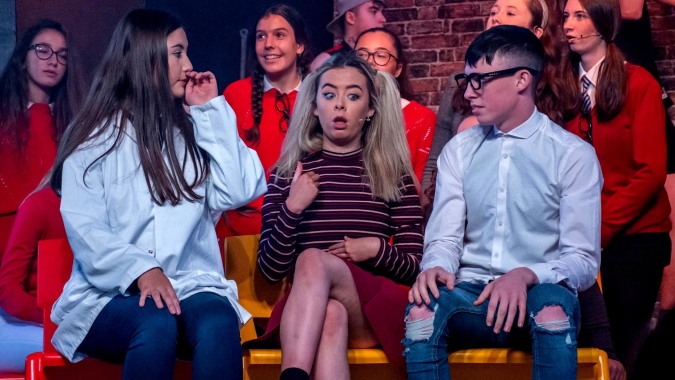 Eine Gruppe Schülerinnen und Schüler der St. Aidan's Comprehensive School sitzt auf der Bühne vor einem bunten Hintergrund.