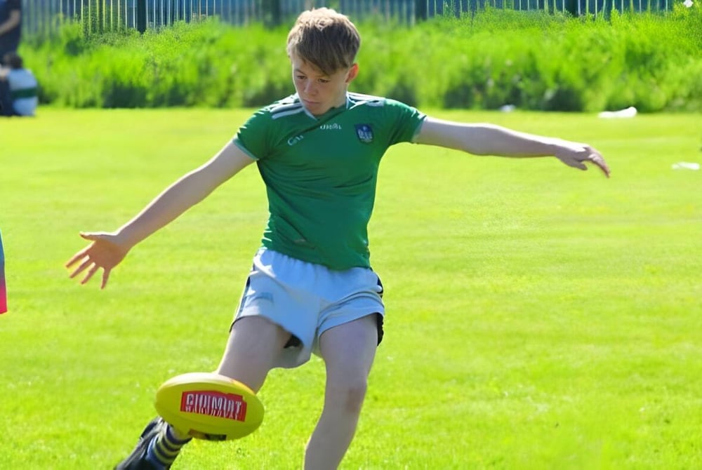 Ein Schüler von St Ailbe's School läuft über ein grasiges Feld und spielt mit einem Fußball.