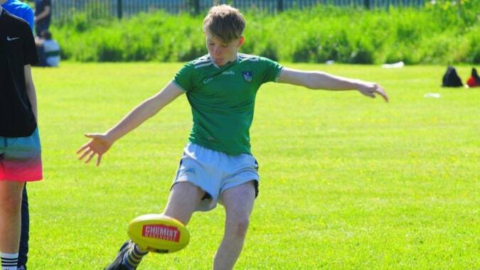 Ein Schüler der St Ailbe's School kickt einen Fußball auf einem Rasenplatz mit Zaun und Bäumen im Hintergrund.