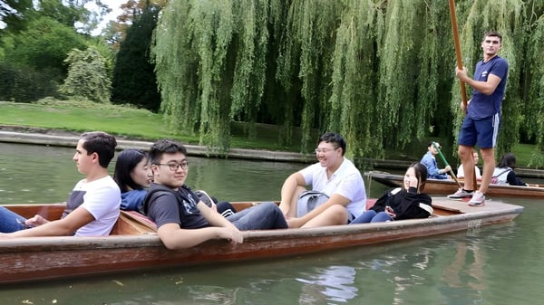 Eine Gruppe Schüler des St. Andrew’s College entspannt in einem Holzboot auf einem Teich mit Weidenbäumen.