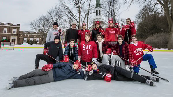 Eine Gruppe Schüler des St. Andrew’s College versammelt sich auf einer Eisbahn mit einer Kirchturmkulisse im Hintergrund.