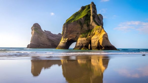 Felsformationen mit grünen und gelben Farben spiegeln sich im ruhigen Wasser am Strand nahe St. Andrew's College.