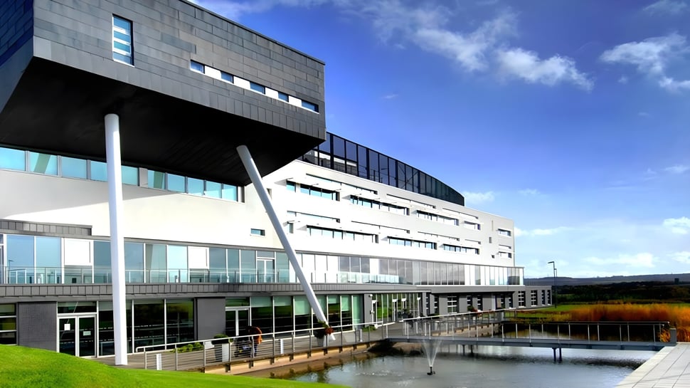 Das moderne Gebäude des St. Andrew's College steht vor einem Teich und ist von grüner Vegetation umgeben.
