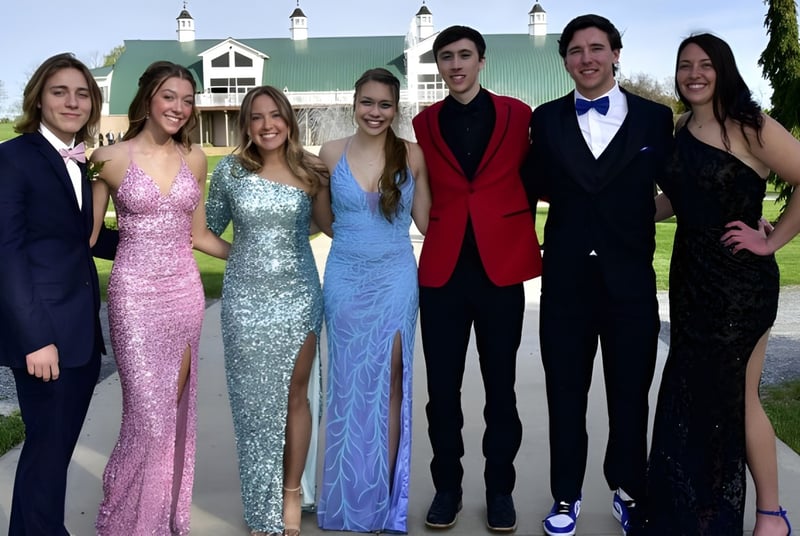 Eine Gruppe von Personen steht vor dem historischen Haupteingang des St. Andrew's College, umgeben von grüner Landschaft.