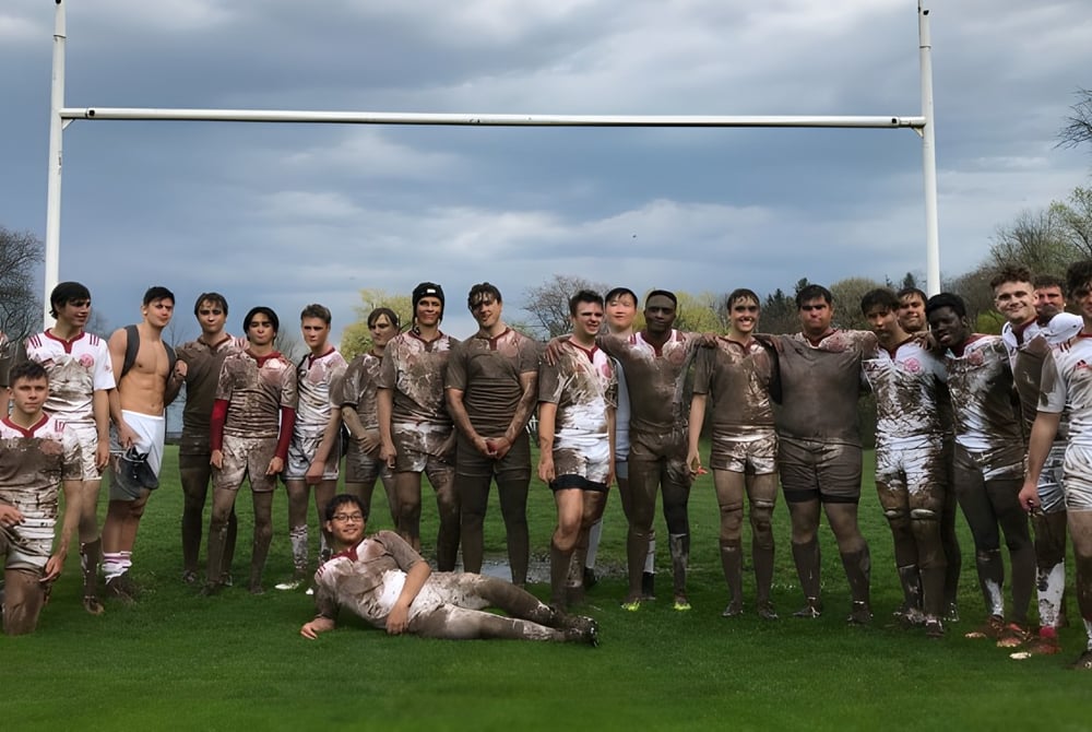 Eine Gruppe von mit Schlamm bedeckten Schülern steht vor einem Rugby-Tor auf dem Sportplatz des St. Andrew’s College.