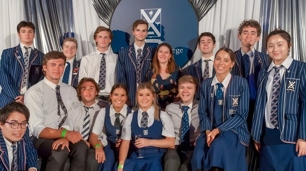 Eine Gruppe Schülerinnen und Schüler in Schuluniform posiert vor einem Hintergrund mit dem Logo von St. Andrew's College.