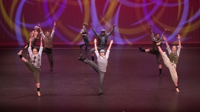 Eine Gruppe von Schülerinnen und Schülern des St. Andrew's College führt eine Tanzaufführung unter violett-orangefarbener Bühnenbeleuchtung auf.
