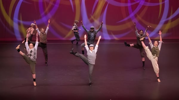 Eine Gruppe von Tänzerinnen und Tänzern führt auf der Bühne im St. Andrew's College vor farbig beleuchtetem Hintergrund auf.