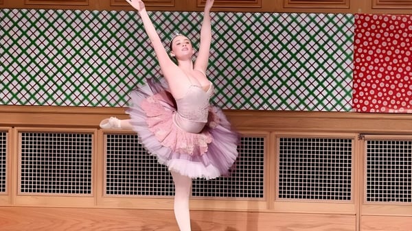 Eine Ballerina in rosa Tutu und Trikot führt vor einem farbenfrohen Muster eine elegante Tanzpose auf der St. Andrew's School vor.