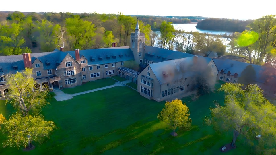 Die historische Schlossartige Architektur der St. Andrew's School steht auf einer grünen Wiese mit Wald und See im Hintergrund.