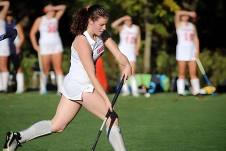 Eine Schülerin der St. Andrew's School läuft in Sportkleidung über ein grünes Spielfeld mit weiteren Spielerinnen im Hintergrund.