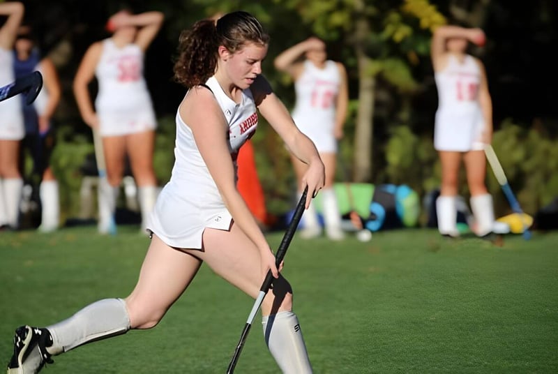 Eine Schülerin der St. Andrew's School läuft in Sportkleidung über ein grünes Spielfeld mit weiteren Spielerinnen im Hintergrund.