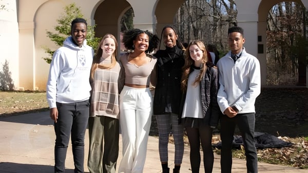 Eine Gruppe von Schülerinnen und Schülern steht vor einem Gebäude mit Rundbogenfenstern auf dem Gelände der St. Andrew's-Sewanee School.