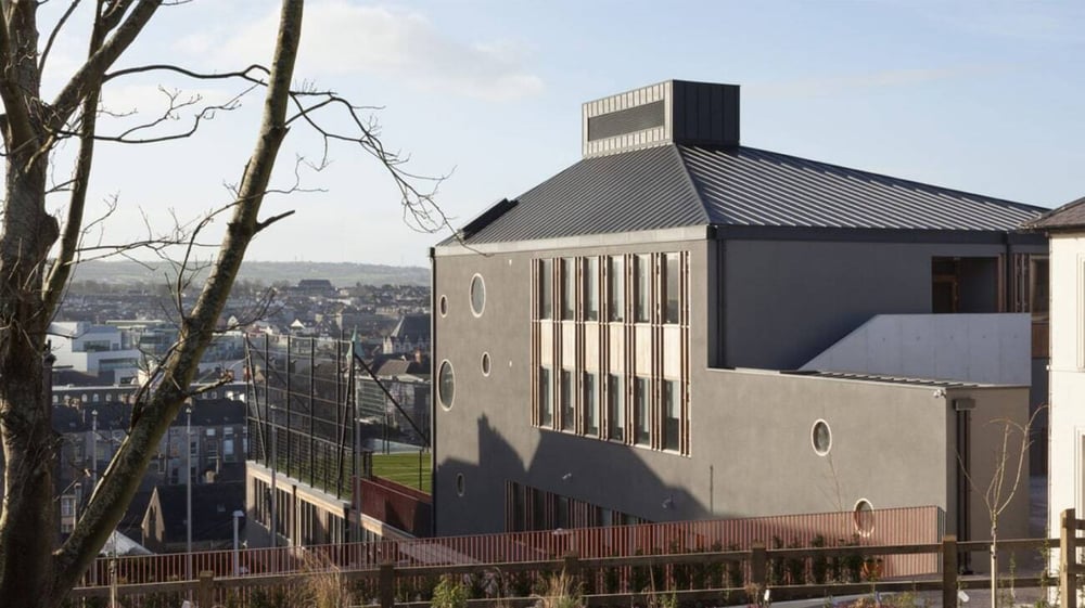 Das moderne Gebäude mit markanter Dachlinie auf dem Campus von St. Angela’s College mit Blick auf die Stadt im Hintergrund.