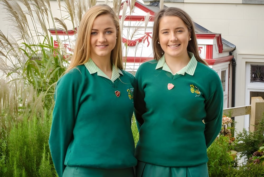 Zwei Schülerinnen in grüner Schuluniform stehen im Garten auf dem Gelände des St. Angela’s College.
