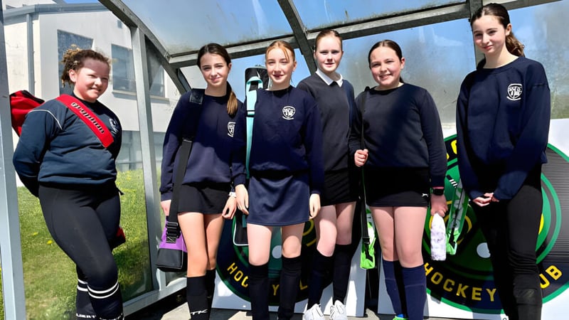 Eine Gruppe von Schülerinnen steht vor einem Gewächshaus auf dem Campus von St. Angela’s College, im Hintergrund ist Sportgerät zu sehen.