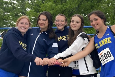 Fünf Schülerinnen der St. Anne Catholic High School stehen in Sportkleidung im Freien vor grüner Kulisse und lächeln in die Kamera.