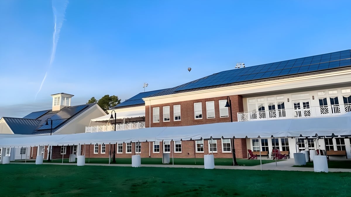 Das mehrstöckige Backsteingebäude der St. Anne's-Belfield School mit Solarpaneelen auf dem Dach und umliegendem Rasen unter blauem Himmel.