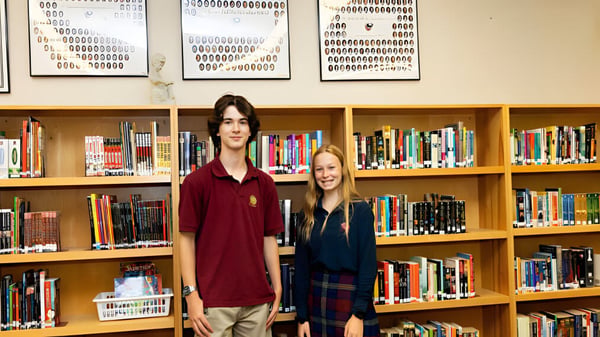 Zwei Schülerinnen und Schüler stehen vor einem Bücherregal in der Bibliothek der St. Anne's Catholic School.