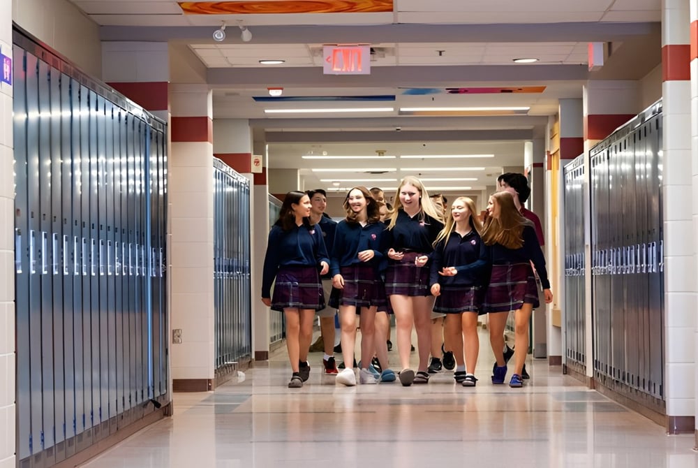 Eine Gruppe junger Schülerinnen in Schuluniformen geht zusammen den hell beleuchteten Flur der St. Anne's Catholic School entlang.