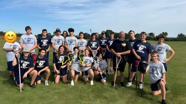 Eine Gruppe von Schülerinnen und Schülern der St. Anne's Catholic School posiert gemeinsam auf einem Sportfeld bei blauem Himmel.