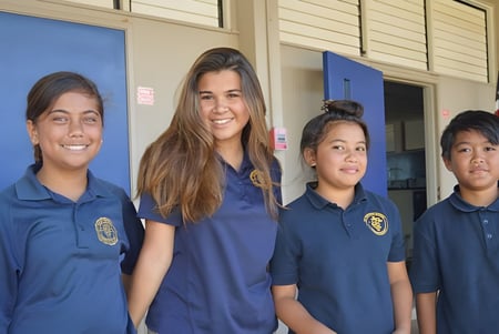 Vier Schüler der St. Anthony School stehen vor einem Gebäude mit blauen und weißen Wänden.