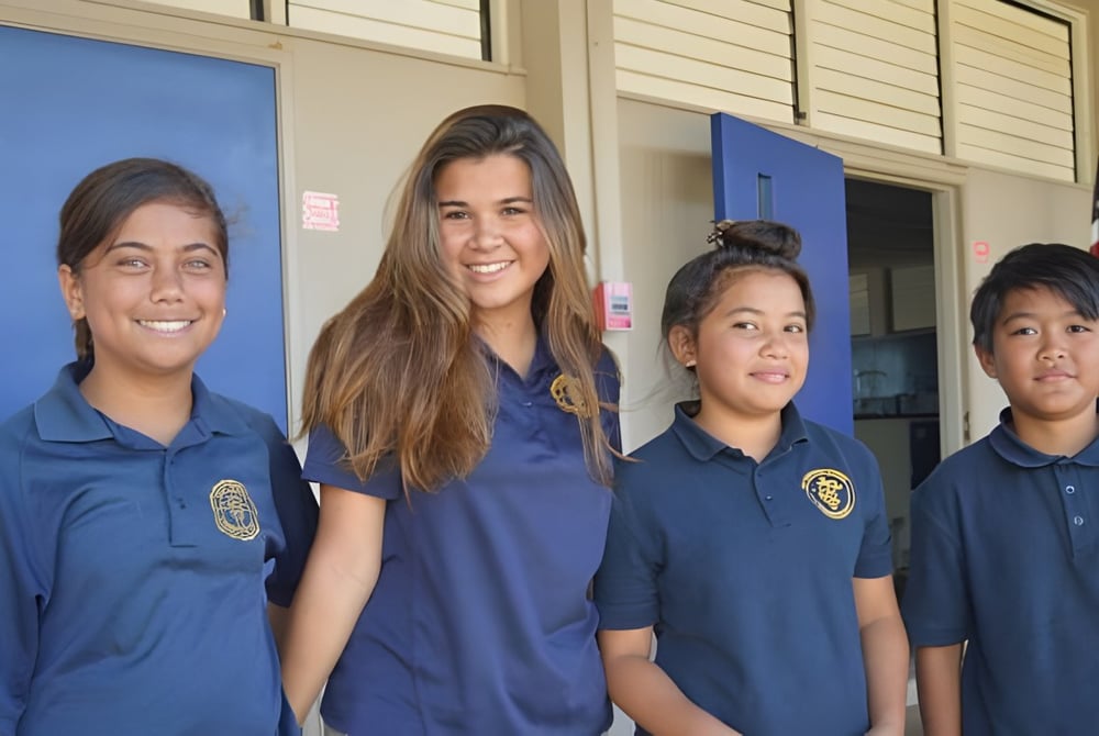 Vier Schüler der St. Anthony School stehen vor einem Gebäude mit blauen und weißen Wänden.
