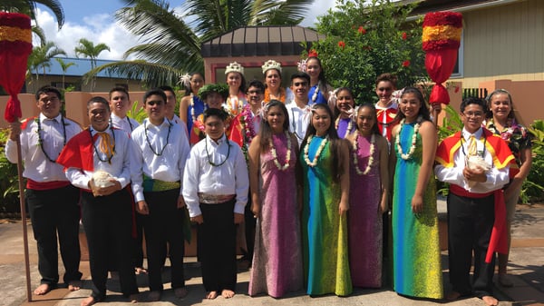 Eine Gruppe von Schülern der St. Anthony School trägt traditionelle Kleidung vor einer tropischen Kulisse mit Palmen.