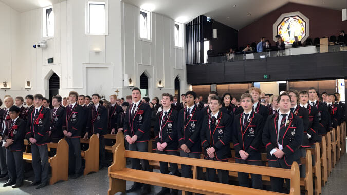 Eine Gruppe von Schülerinnen und Schülern des St. Bede's College sitzt in formeller Kleidung in der Kirche bei einem Auftritt.
