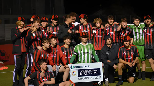 Eine Gruppe junger Fußballspieler mit roten und schwarzen Trikots feiert den Meisterschaftssieg auf dem Spielfeld des St. Bede's College.