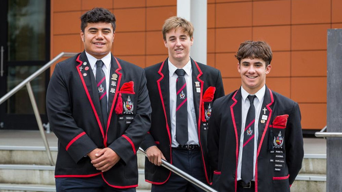 Drei Schüler in Schuluniform stehen zusammen auf der Treppe eines Gebäudes auf dem Campus von St. Bede's College.