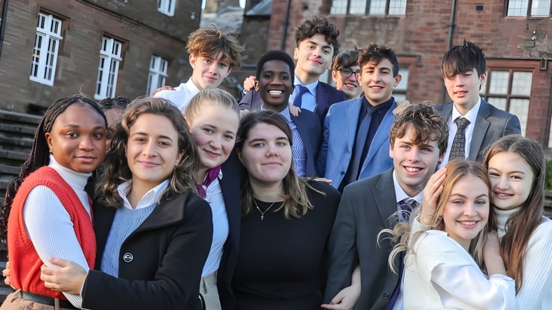 Eine Gruppe von Schülerinnen und Schülern steht lächelnd vor einem Backsteingebäude der St. Bees School.