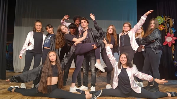 Eine Gruppe von Schülern der St. Bees School posiert gemeinsam auf einer Bühne mit dunklem Hintergrund.