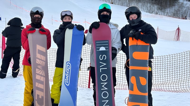 Eine Gruppe Schülerinnen und Schüler der St. Benedict Catholic Secondary School trägt bunte Skikleidung und steht vor einer schneebedeckten Piste.