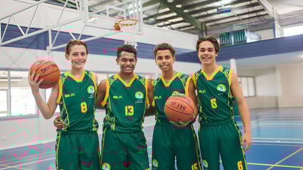 Vier Schüler des St. Brendan's College stehen auf dem Basketballfeld in grünen Trikots zusammen.