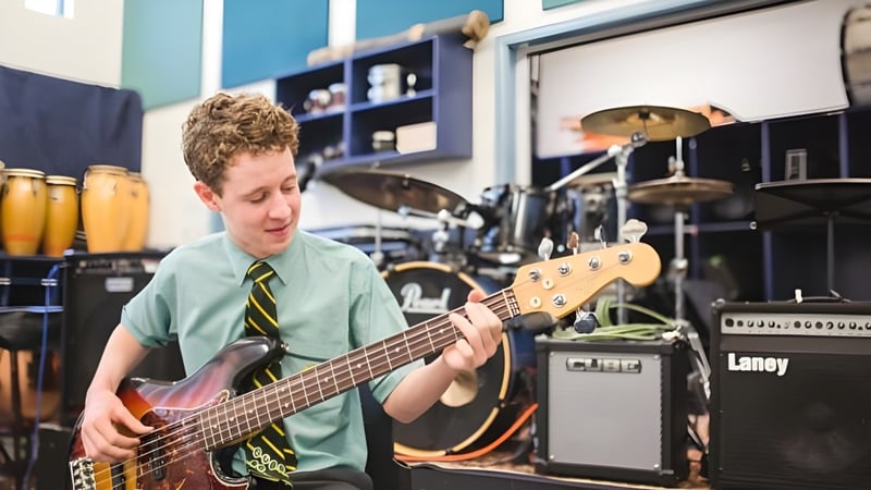 Ein Schüler des St. Brendan's College spielt E-Gitarre in einem Musikstudio mit Musikinstrumenten im Hintergrund.