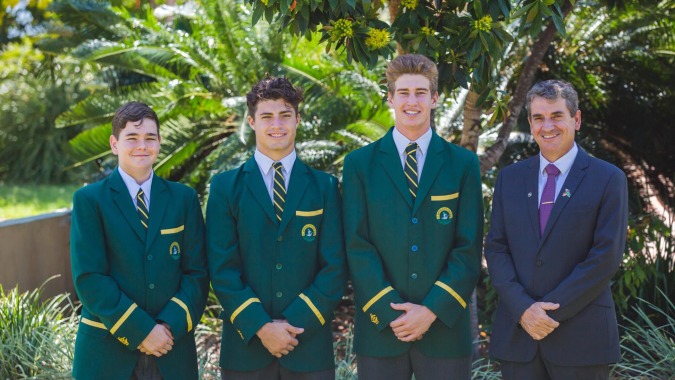 Vier Schüler in grünen und violetten Schuluniformen stehen gemeinsam im tropischen Garten auf dem Campus von St. Brendan's College.