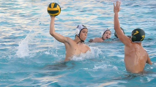 Zwei Schüler der St. Brendan’s Community School spielen Volleyball im Schwimmbecken bei sonnigem Wetter.