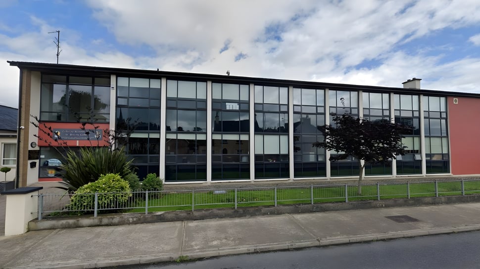 Das mehrstöckige Gebäude des St. Bricin’s College mit großen Glasfenstern steht vor einer grasbewachsenen Fläche unter bewölktem Himmel.