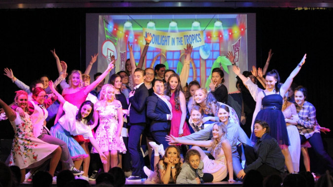 Schülerinnen des St. Brigid's College stehen bei einem Bühnenauftritt vor farbenfrohen Hintergründen.